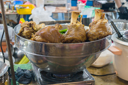 Close-up of tender braised pork trotters with glossy brown skin and exposed bones arranged in a stainless steel bowl at a local food stall.
