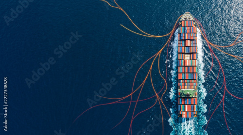 Aerial view of a massive cargo ship with colorful containers sailing through blue ocean, with abstract network lines, ideal for logistics, global trade and shipping industry
