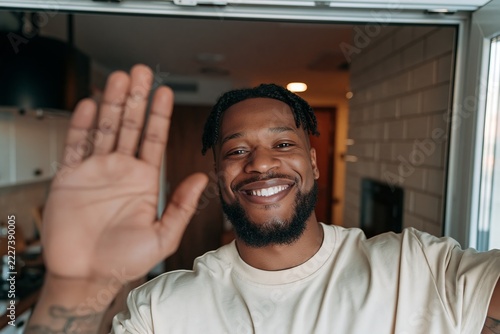 Happy bearded man waving hand at camera while making video call indoors at home kitchen setting