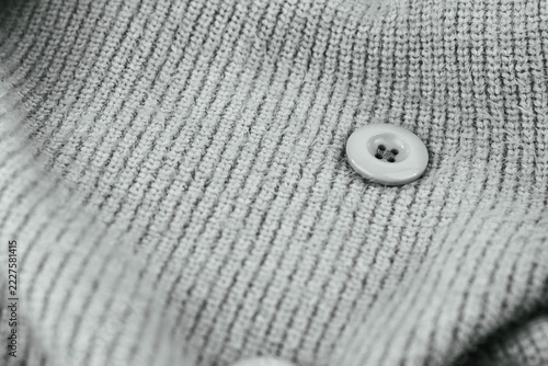 Monochrome image, knitted synthetic material sweater with button close up shot.