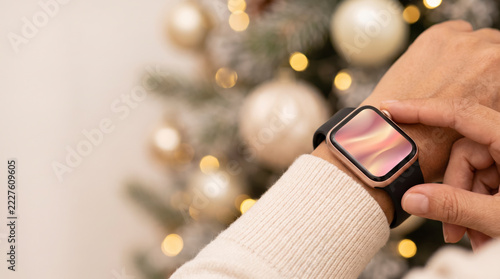 Mindful wearer tapping a rose gold smartwatch beside a flocked Christmas tree with cream ornaments