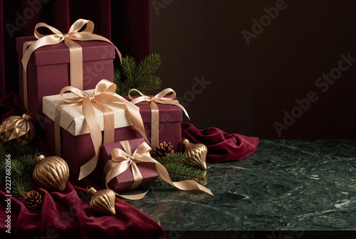 Wrapped gifts sit on a dark marble surface with green branches and ornaments during the holiday season