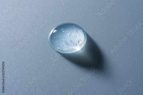 Clear cosmetic gel drop with dramatic shadow on blue