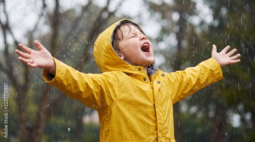 Joyful young boy wearing vibrant yellow raincoat playing outside in rain
