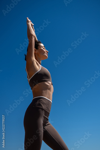 Athletic woman stretching outdoors against blue sky, fitness lifestyle concept, toned body, flexibility exercise, healthy skin, active movement, sunny summer day, minimal background