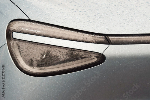 A view of a modern car's headlight covered in raindrops