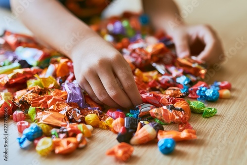 Child hands picking colorful wrapped candies from a pile on wooden floor