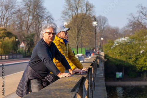 Photography Two senior men standing on a bridge in london, enjoying the view in a park on a