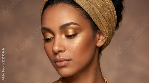 Beautiful young woman with luxury golden makeup and sparkling headband in beauty portrait. Concept of metallic makeup, gold eyeshadow, african american woman, beauty model, skincare, luxury cosmetics.