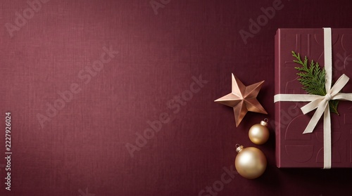 Top view of a luxury Christmas gift box on burgundy fabric background. Flat lay of holiday present with gold ornaments and copy space