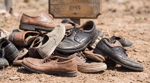 Pile of worn shoes on dry ground beneath wooden sign marked 1945. World War II remembrance and historical memorial. Loss, conflict and peace concept. Memorial tribute.