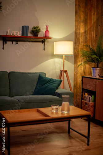 Tall lamp casting warm glow accenting midcentury sofa, plant silhouette, textured wall, curated shelf accessories, atmospheric hotelstyle mood for commercial imagery