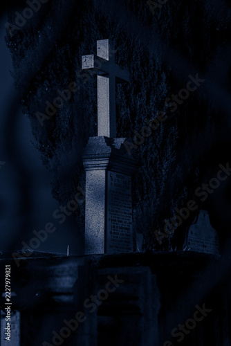 Stone cross headstone grave monument in graveyard under dark blue moonlight