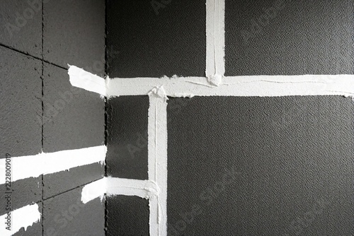 Construction worker installs cement backer boards in bathroom corner. White mortar fills gaps between dark gray waterproof panels during home remodel. New wall structure prepared for tile