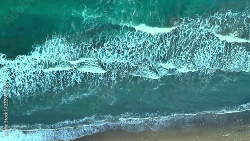 Aerial view of turquoise ocean waves crashing on sandy beach shore