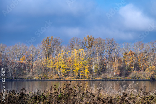 Autumn landscape with moody sky and far riverbank, illuminated by sunbeams.