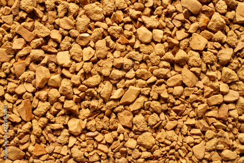 Detailed macro background texture of brown freeze-dried instant coffee granules. Full frame view of soluble coffee particles showing natural rough structure and pattern.