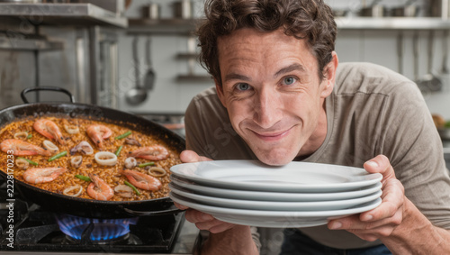 Man holding plates by fresh seafood paella, illustrating Spanish cuisine, home cooking, meal preparation, food presentation, Mediterranean cuisine, and traditional family meal