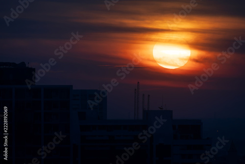 dramatic city view, blazing golden sun, over dark silhouettes of urban high-rises, illuminating wispy layers of clouds in fiery orange, deep red, and dark amber hues during twilight, sunrise or sunset