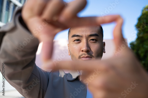Man framing his face with hands outdoors under blue sky in Madrid