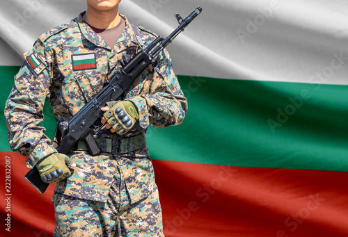 Fotografie Bulgaria flag with soldier in military uniform holding assault rifle in front of