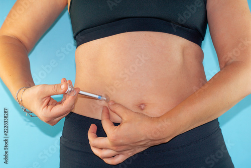 woman injecting syringe into belly in sportswear on blue background, close up of abdomen concept of testosterone therapy, anabolic steroids for muscle growth and weight loss, fitness, bodybuilding
