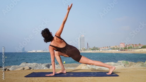Flexible woman practicing yoga twist lunge on the beach