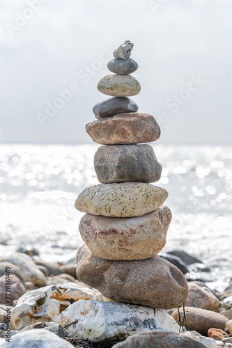 Gestapelter Steinturm balanciert präzise am kiesigen Ostseestrand vor glitzerndem, hellem Meerwasser in ruhiger, meditativer Sommeratmosphäre als authentisches Symbol für Balance.