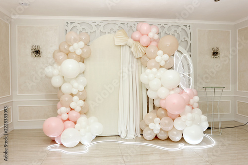 A celebration photo area features an arch of white, cream, and pale pink balloons, light curtains, and decorative lighting.