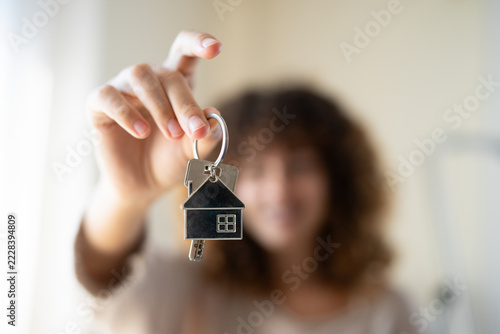Keys with house-shaped keychain held indoors with blurred white person