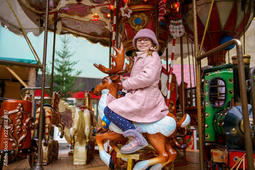 Little school girl riding on a merry go round carousel at Christmas funfair or market, outdoors. Happy child having fun on traditional family xmas market in Germany