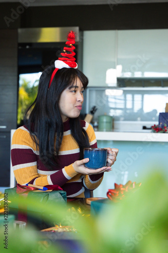 Woman sitting at kitchen table holding blue mug, wearing red spiral headband, observing gifts