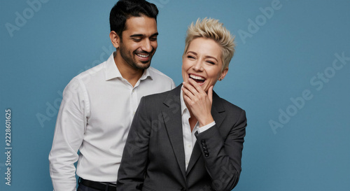Young man standing behind laughing woman in stylish suits against blue background  