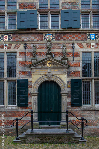 View of the historic brick facade of the Naarden-Vesting building, featuring an ornate stone doorway, green shutters, and decorative statues in Naarden, Noord-Holland, Netherlands.