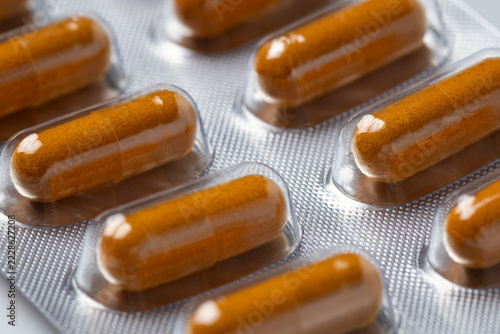 transparent gelatin capsules filled with orange-brown powder organized neatly inside reflective silver metallic blister pack, presenting a clean and clinical look, Turmeric capsules in blister pack