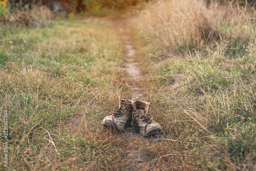 Pair of old worn shabby shoes with dusty cracked leather and untied laces standing in dry grass