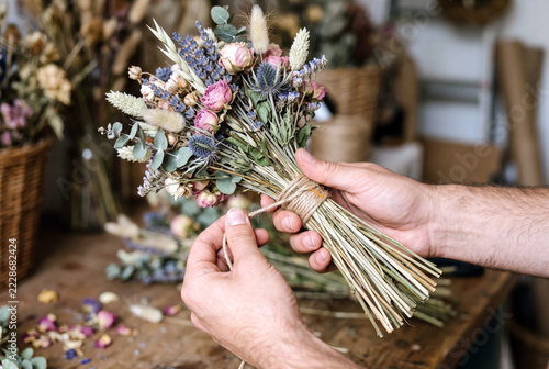Close-up of a florist's hands tying a bouquet of colorful dried flowers and lavender with natural jute twine cord.