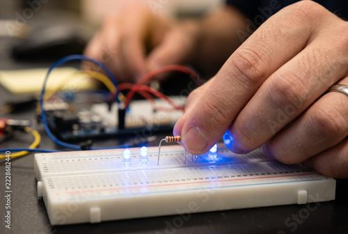 Close-up of an engineer placing a resistor onto a breadboard circuit with lit blue LED lights during a science experiment.