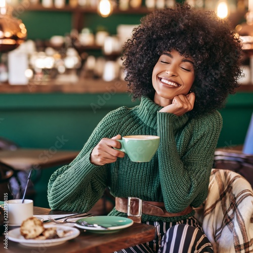 Young black woman with afro hairstyle smiling and drinking coffee in cafe indoors 