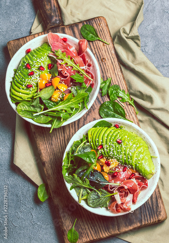 Keto Low carbs bowl. Fresh salad with green spinach, rucola, avocado an ham serrano on gray background