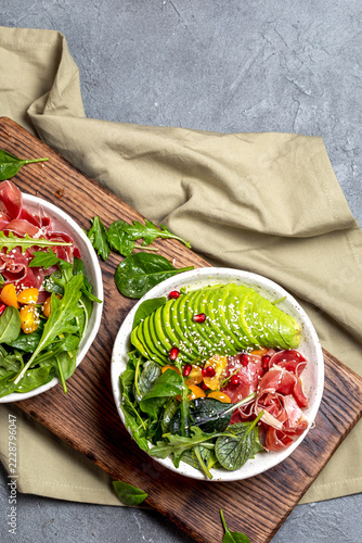 Keto Low carbs bowl. Fresh salad with green spinach, rucola, avocado an ham serrano on gray background