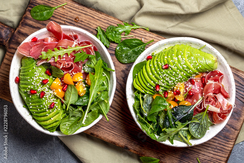 Keto Low carbs bowl. Fresh salad with green spinach, rucola, avocado an ham serrano on gray background