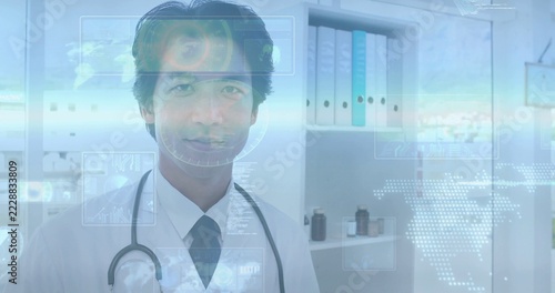 Standing Japanese doctor wearing white coat, dark tie in clinic, with stethoscope, holograms