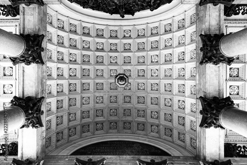 Grand circular ceiling with intricate tile patterns. Symmetrical design features ornate columns and detailed motifs. Monochrome tones highlight architectural elegance and historical grandeur