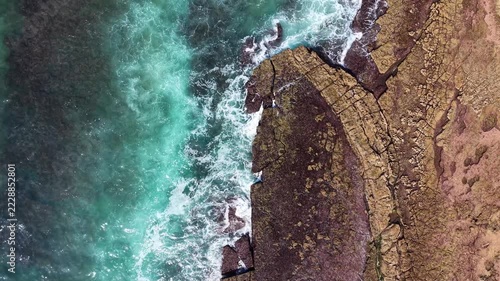 An aerial view of turquoise ocean waves crashing against a rocky shoreline