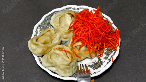 Traditional steamed manti dumplings topped with spicy Korean carrot salad served on a plate with a fork