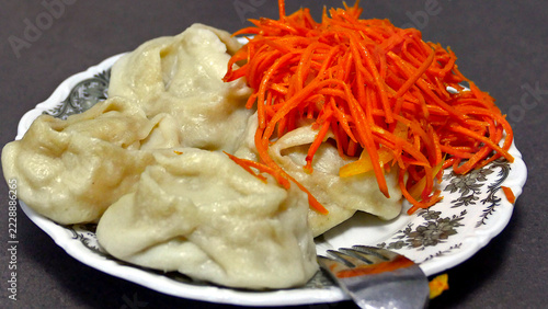 Traditional steamed manti dumplings topped with spicy Korean carrot salad served on a plate with a fork