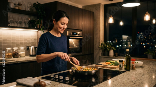 Woman happily cooking healthy food in modern kitchen at night with city view