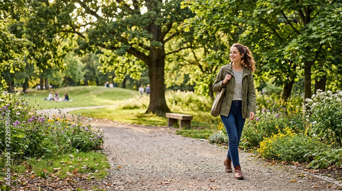 Woman walking on park path enjoying nature and sunlight