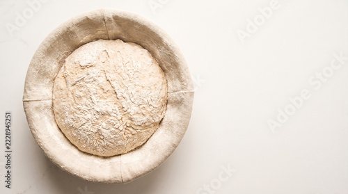 Bread dough proofing in bowl with flour, overhead view, rustic baking preparation and neutral background